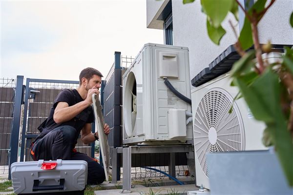 Heat pump repair technician diagnosing an outdoor unit